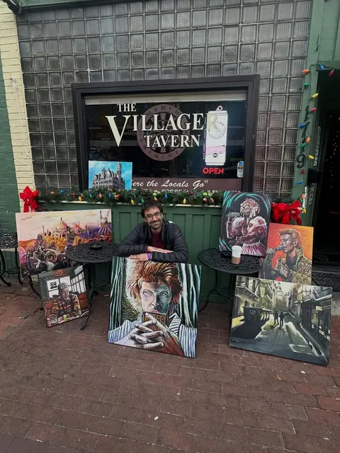Toby at a sidewalk table outside The Villager Tavern surrounded by his paintings